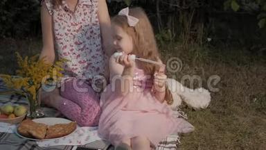 一对幸福的母女给肥皂泡充气.. 一家人在城市公园里，在日落的温暖的晚上野餐。